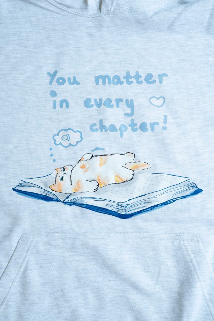 Drawing of ginger and white cat lying on an open book, dreaming of fish. The caption states "You matter in every chapter!" with the image of a heart
